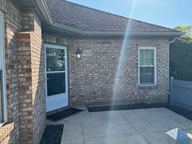 doorway to property with a patio, a shingled roof, and brick siding