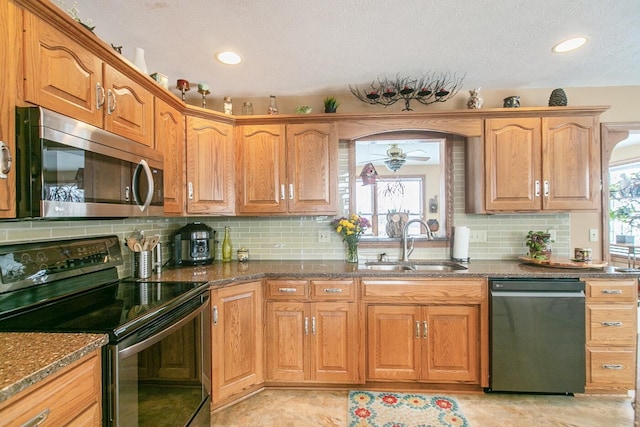 kitchen featuring sink, tasteful backsplash, dark stone counters, ceiling fan, and stainless steel appliances