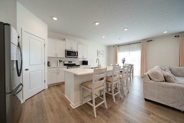 kitchen featuring an island with sink, appliances with stainless steel finishes, white cabinets, a breakfast bar, and sink