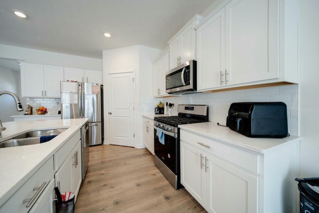 kitchen with backsplash, sink, light wood-type flooring, stainless steel appliances, and white cabinets