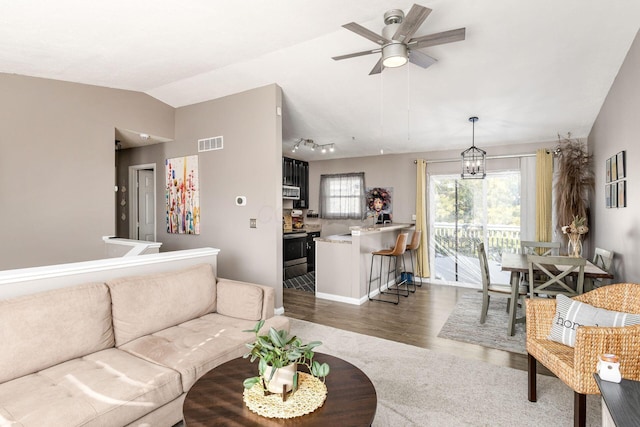 living room with vaulted ceiling, dark wood-type flooring, ceiling fan with notable chandelier, and sink