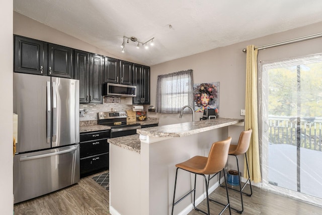 kitchen with tasteful backsplash, a breakfast bar, kitchen peninsula, wood-type flooring, and appliances with stainless steel finishes