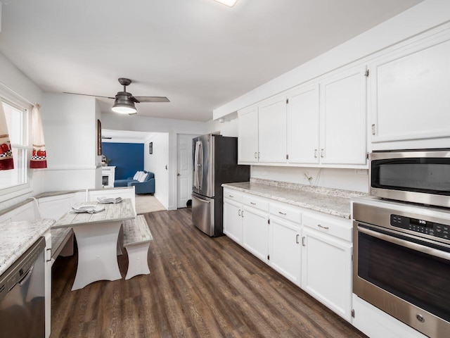 kitchen with white cabinetry, appliances with stainless steel finishes, dark hardwood / wood-style floors, ceiling fan, and light stone countertops