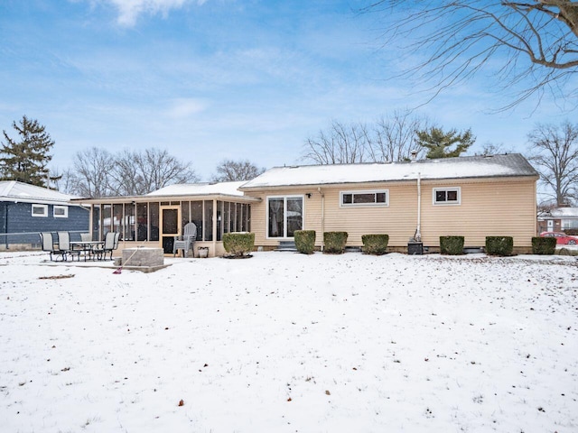 snow covered rear of property with a sunroom