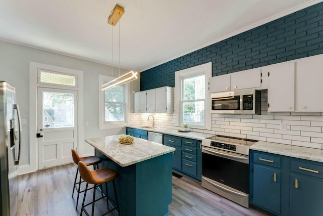 kitchen with pendant lighting, appliances with stainless steel finishes, a center island, white cabinetry, and sink