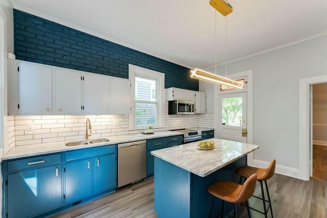 kitchen featuring pendant lighting, appliances with stainless steel finishes, a center island, white cabinetry, and sink