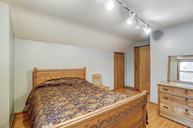 bedroom with vaulted ceiling, track lighting, and light hardwood / wood-style floors