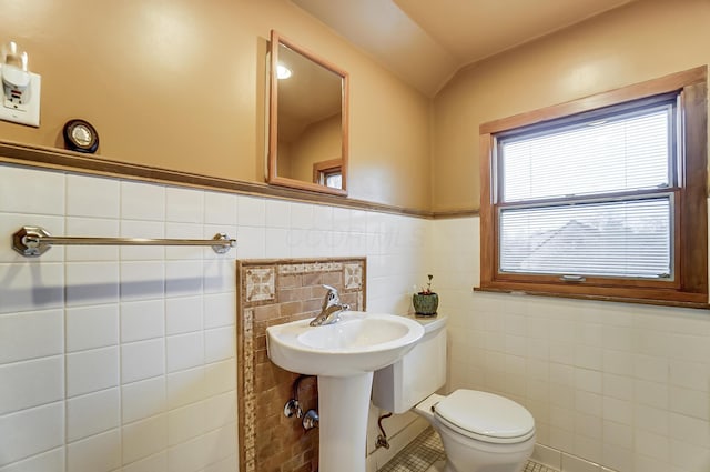 bathroom with toilet, sink, and tile walls