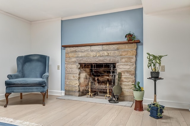 sitting room featuring hardwood / wood-style floors, crown molding, and a stone fireplace