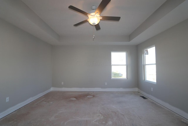 empty room with ceiling fan and a raised ceiling