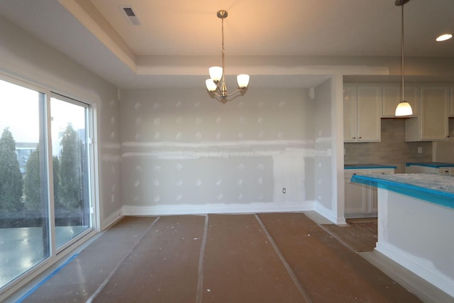 unfurnished dining area featuring a tray ceiling and an inviting chandelier