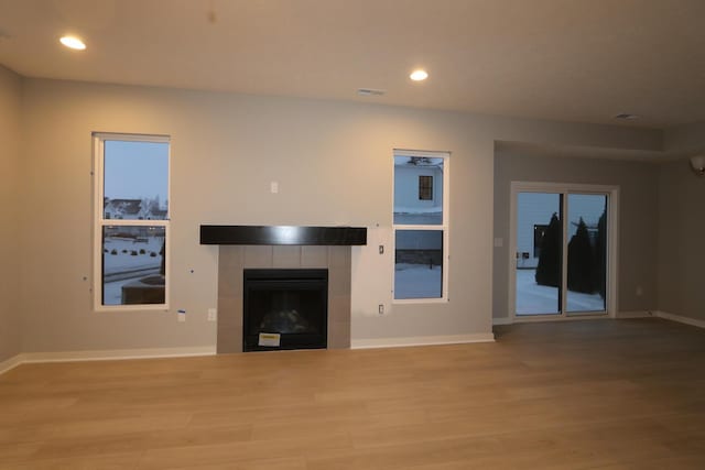 unfurnished living room with ceiling fan, a tiled fireplace, and light wood-type flooring