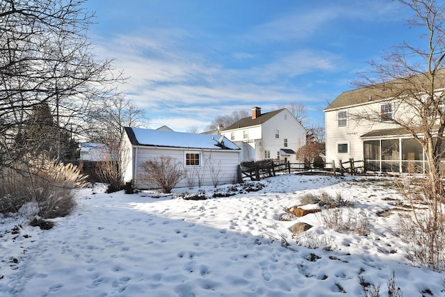 snow covered rear of property featuring a sunroom