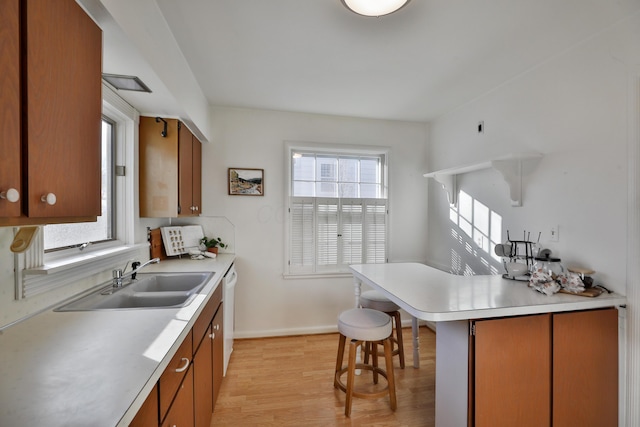 kitchen featuring a kitchen breakfast bar, kitchen peninsula, white dishwasher, sink, and light wood-type flooring