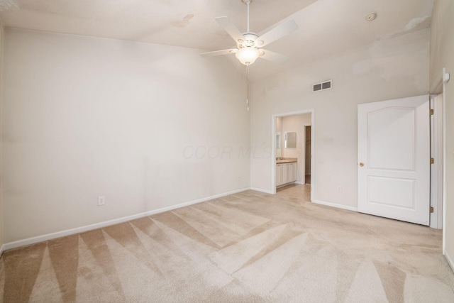 unfurnished bedroom featuring ceiling fan, a high ceiling, ensuite bathroom, and light carpet