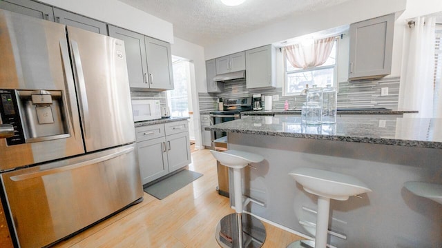 kitchen featuring stainless steel appliances, gray cabinets, stone counters, and a textured ceiling