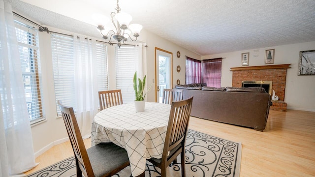 dining room with a chandelier, a textured ceiling, a fireplace, and light hardwood / wood-style flooring