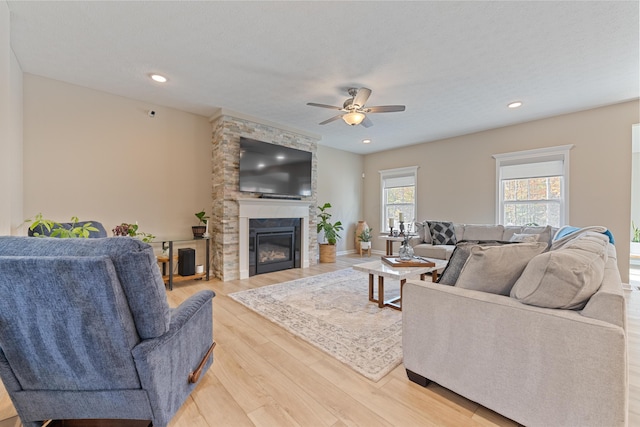 living room featuring ceiling fan, wood-type flooring, a stone fireplace, and a textured ceiling