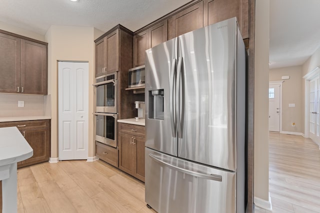 kitchen with dark brown cabinets, stainless steel appliances, light hardwood / wood-style floors, and backsplash