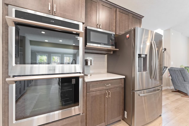 kitchen with light hardwood / wood-style floors, backsplash, dark brown cabinetry, and stainless steel appliances