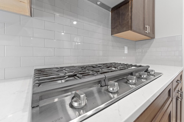 room details featuring stainless steel gas stovetop, backsplash, and light stone counters