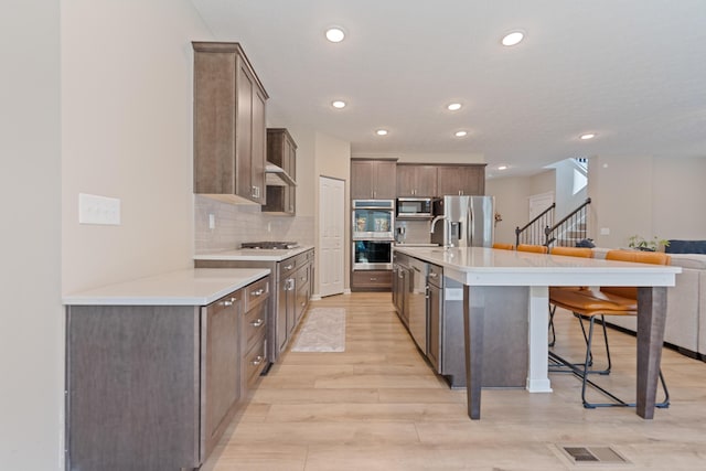 kitchen featuring stainless steel appliances, decorative backsplash, a kitchen breakfast bar, light wood-type flooring, and sink