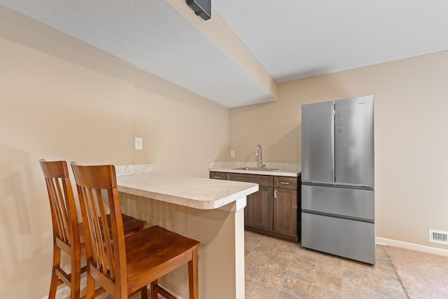 kitchen featuring a breakfast bar, kitchen peninsula, stainless steel refrigerator, and sink