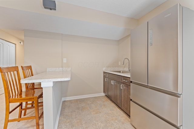 kitchen with kitchen peninsula, sink, dark brown cabinetry, a kitchen breakfast bar, and stainless steel fridge