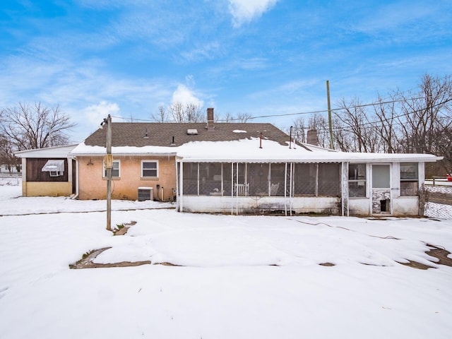 snow covered rear of property featuring central AC and a sunroom