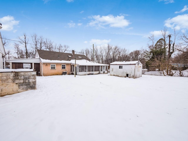 snow covered back of property featuring a sunroom