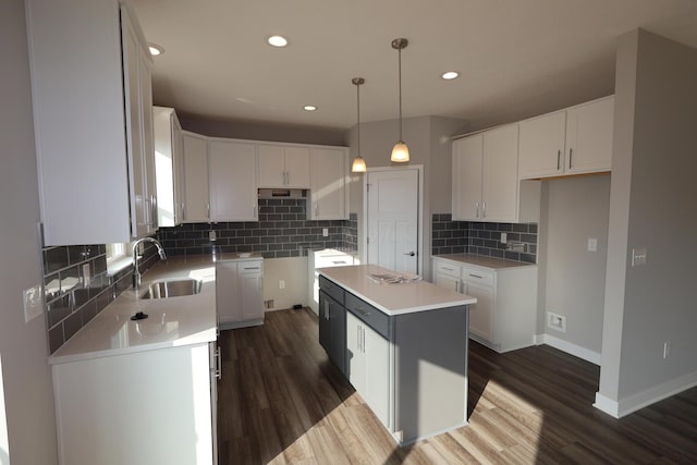 kitchen featuring backsplash, dark wood-type flooring, a kitchen island, a sink, and baseboards