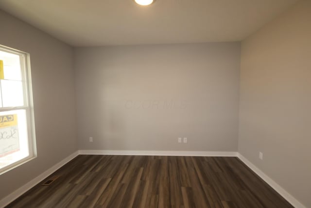 unfurnished room featuring visible vents, dark wood finished floors, and baseboards