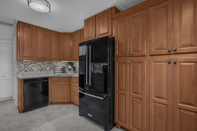 kitchen with light stone counters, backsplash, black appliances, and sink