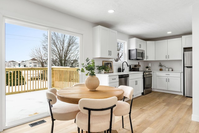 kitchen with white cabinetry, light hardwood / wood-style floors, stainless steel appliances, a textured ceiling, and sink