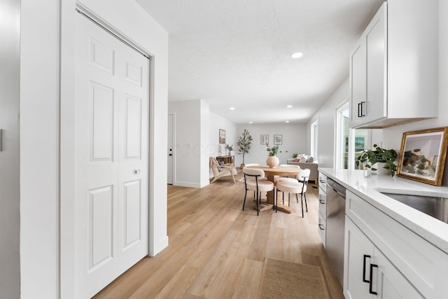 kitchen with white cabinetry, stainless steel dishwasher, a textured ceiling, and light wood-type flooring