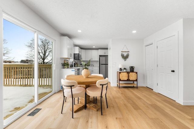 dining space featuring light hardwood / wood-style floors, sink, and a textured ceiling