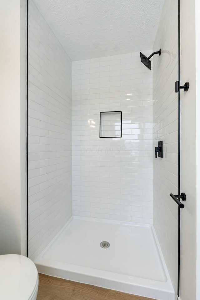 bathroom featuring toilet, a textured ceiling, and tiled shower