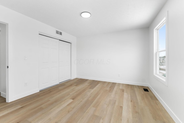 unfurnished bedroom featuring a closet, multiple windows, and light hardwood / wood-style flooring