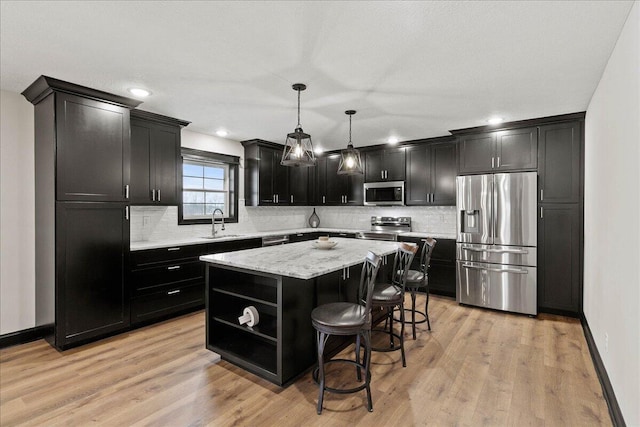 kitchen featuring a kitchen island, stainless steel appliances, sink, hanging light fixtures, and light hardwood / wood-style flooring