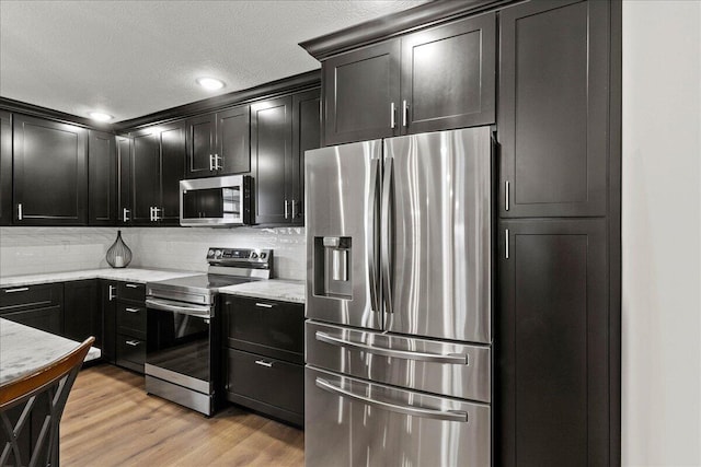 kitchen featuring tasteful backsplash, light hardwood / wood-style flooring, light stone countertops, a textured ceiling, and stainless steel appliances