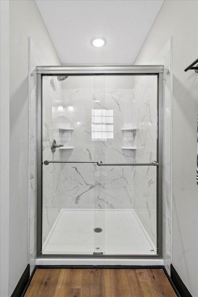 bathroom with a textured ceiling, a shower with shower door, and hardwood / wood-style floors