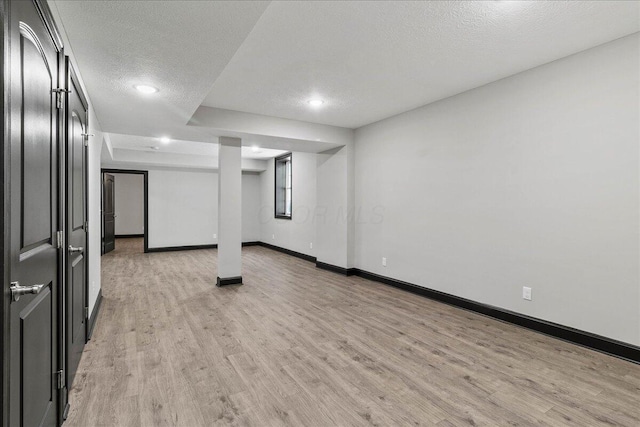 basement featuring light wood-type flooring and a textured ceiling