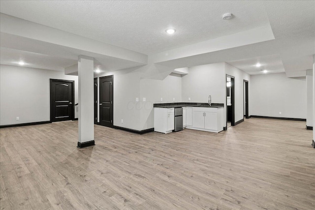 basement with light wood-type flooring, sink, and a textured ceiling