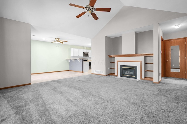 unfurnished living room featuring light carpet, a tiled fireplace, high vaulted ceiling, and ceiling fan