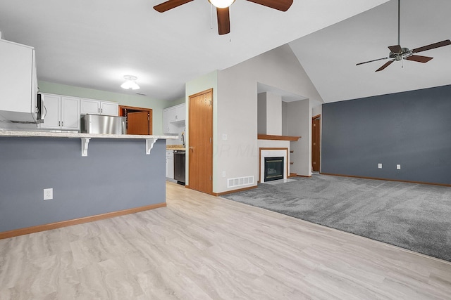 unfurnished living room with a ceiling fan, visible vents, baseboards, lofted ceiling, and a fireplace with flush hearth