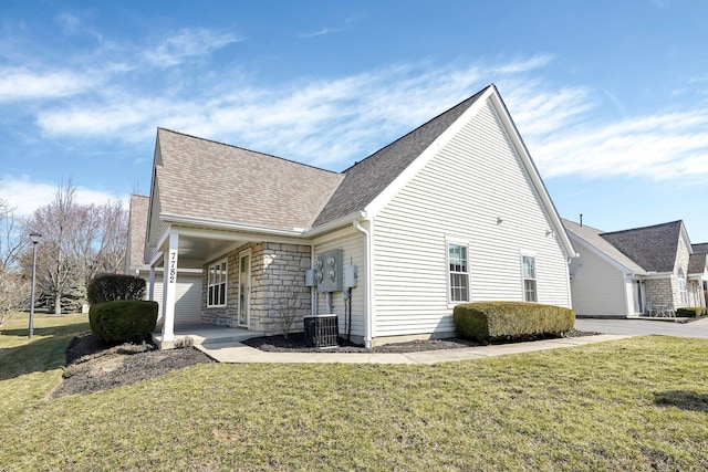 view of property exterior with a yard, stone siding, central AC unit, and a shingled roof