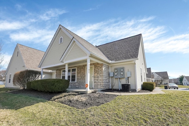 view of front of property with a front yard, a porch, stone siding, and a shingled roof