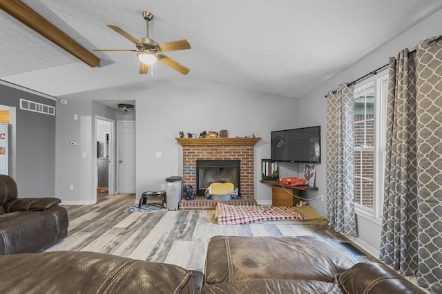 living room featuring ceiling fan, a fireplace, vaulted ceiling with beams, light wood-type flooring, and a textured ceiling