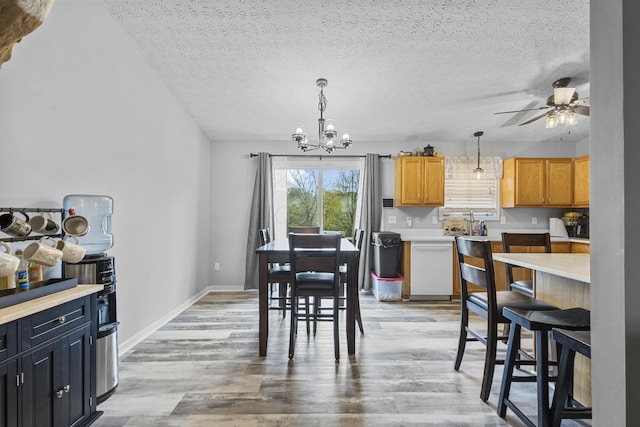 dining area featuring light wood-type flooring, ceiling fan with notable chandelier, and a textured ceiling