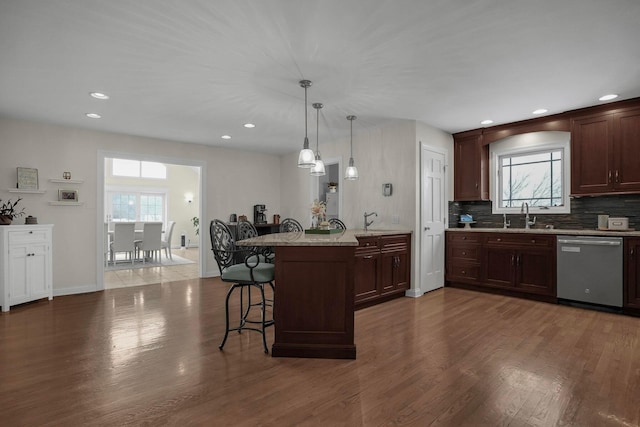 kitchen with stainless steel dishwasher, hanging light fixtures, light stone countertops, plenty of natural light, and a breakfast bar area